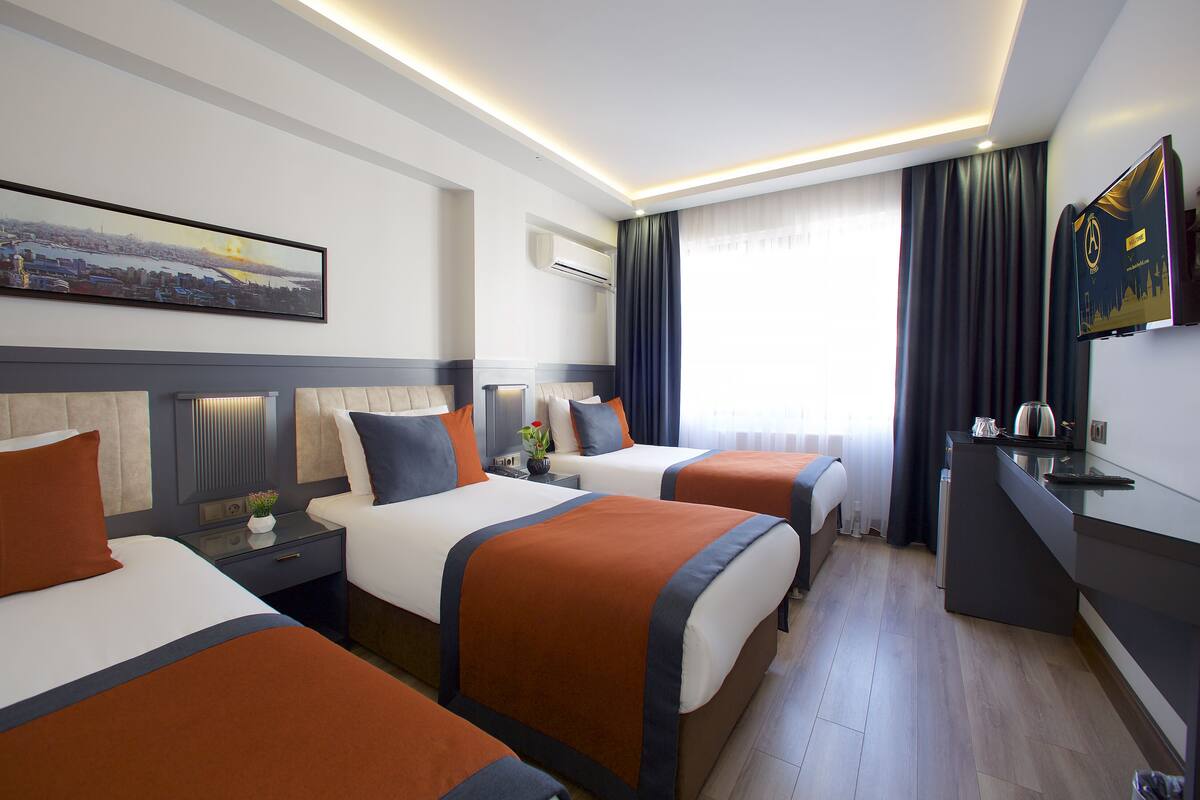 A hotel room with three beds, a desk, and a flat-screen TV.