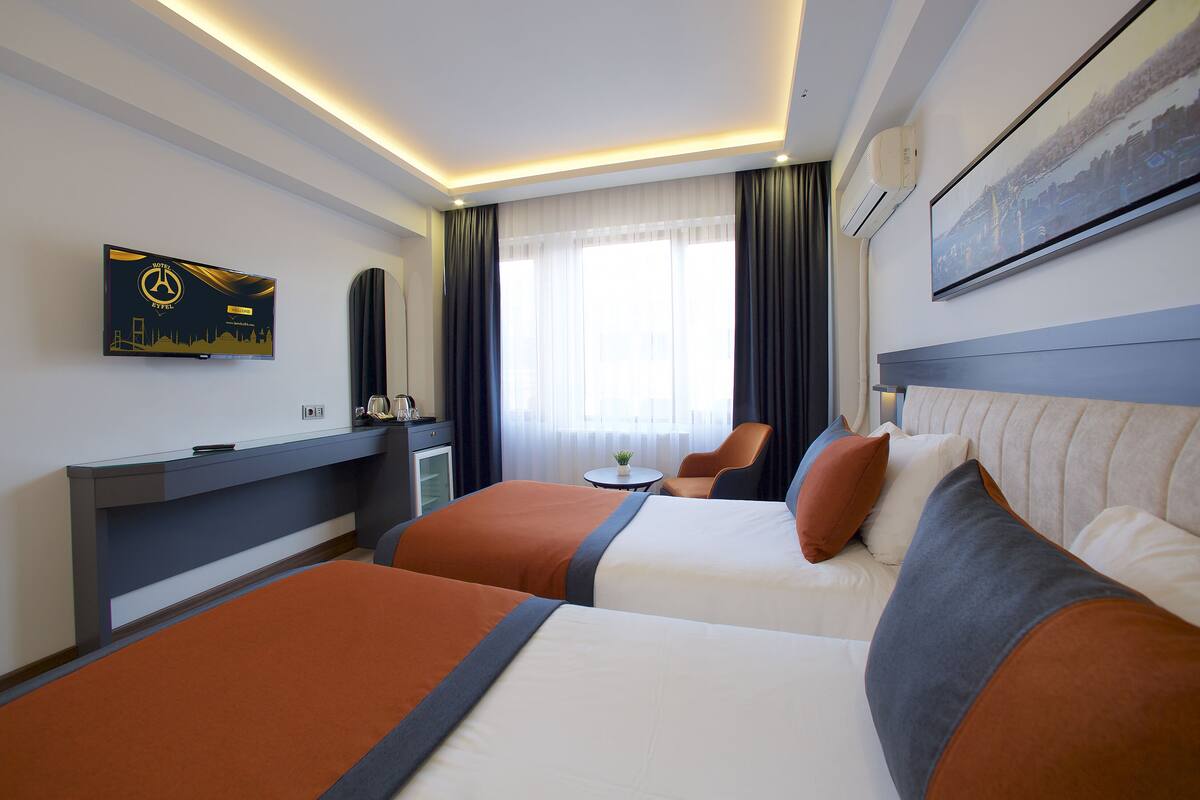 A hotel room with two beds, a desk, a chair, a TV, and a window with curtains.