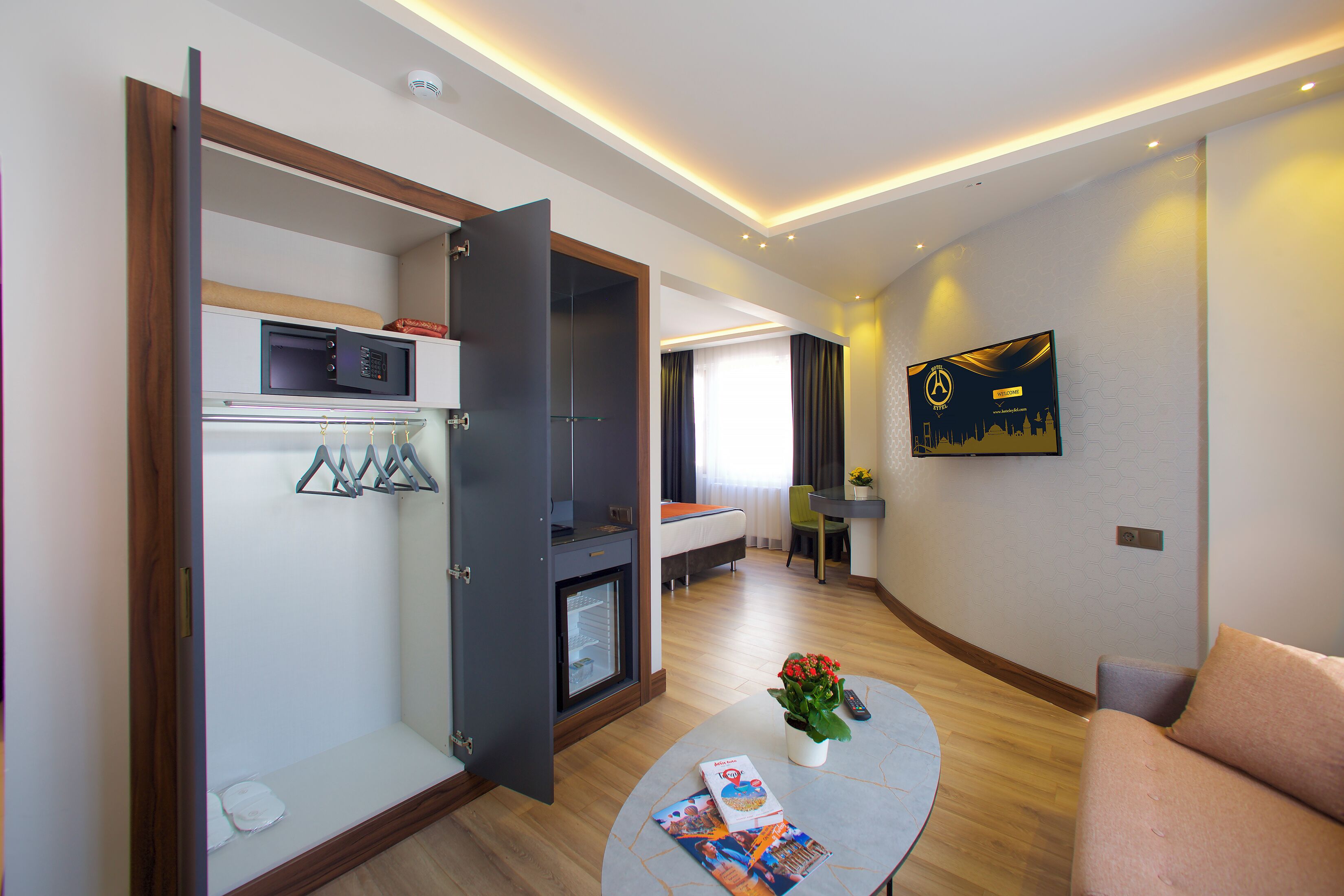 Une chambre d’hôtel comprenant un lit, un coin salon avec une table, un petit réfrigérateur et un téléviseur fixé au mur.