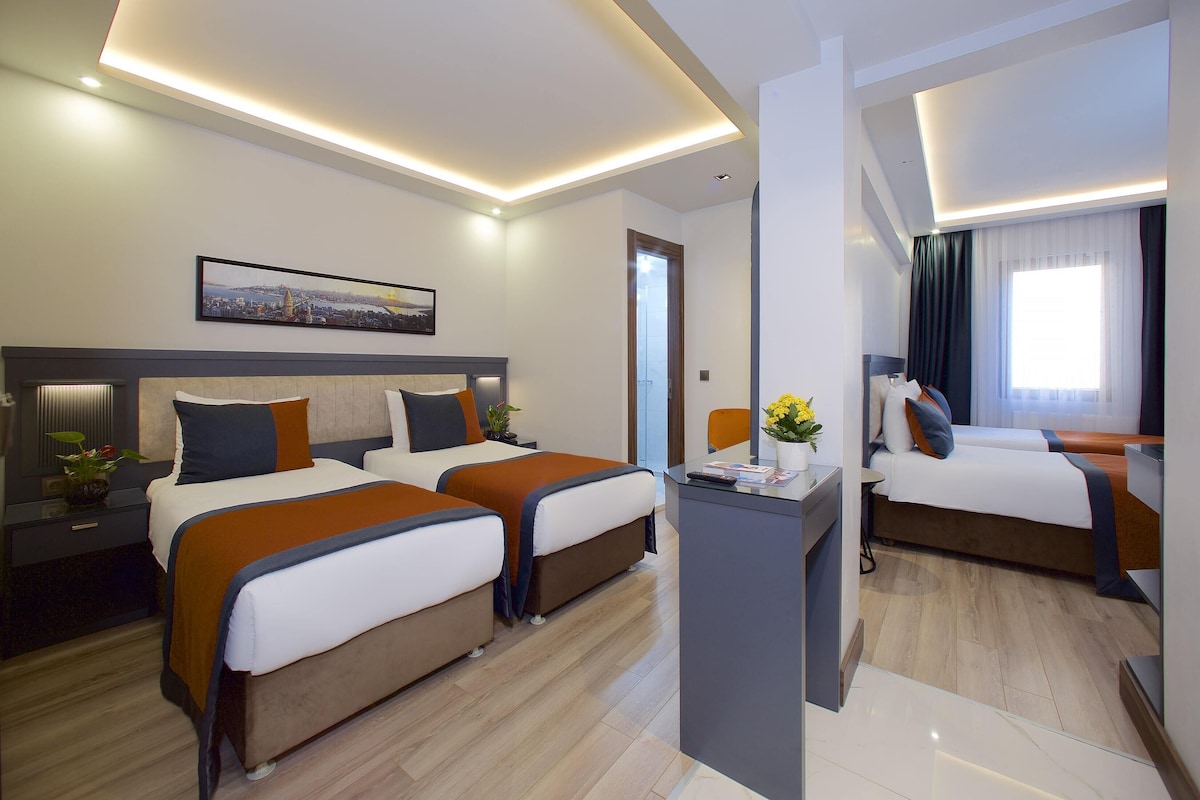 A hotel room with two beds, a desk, and a large window.