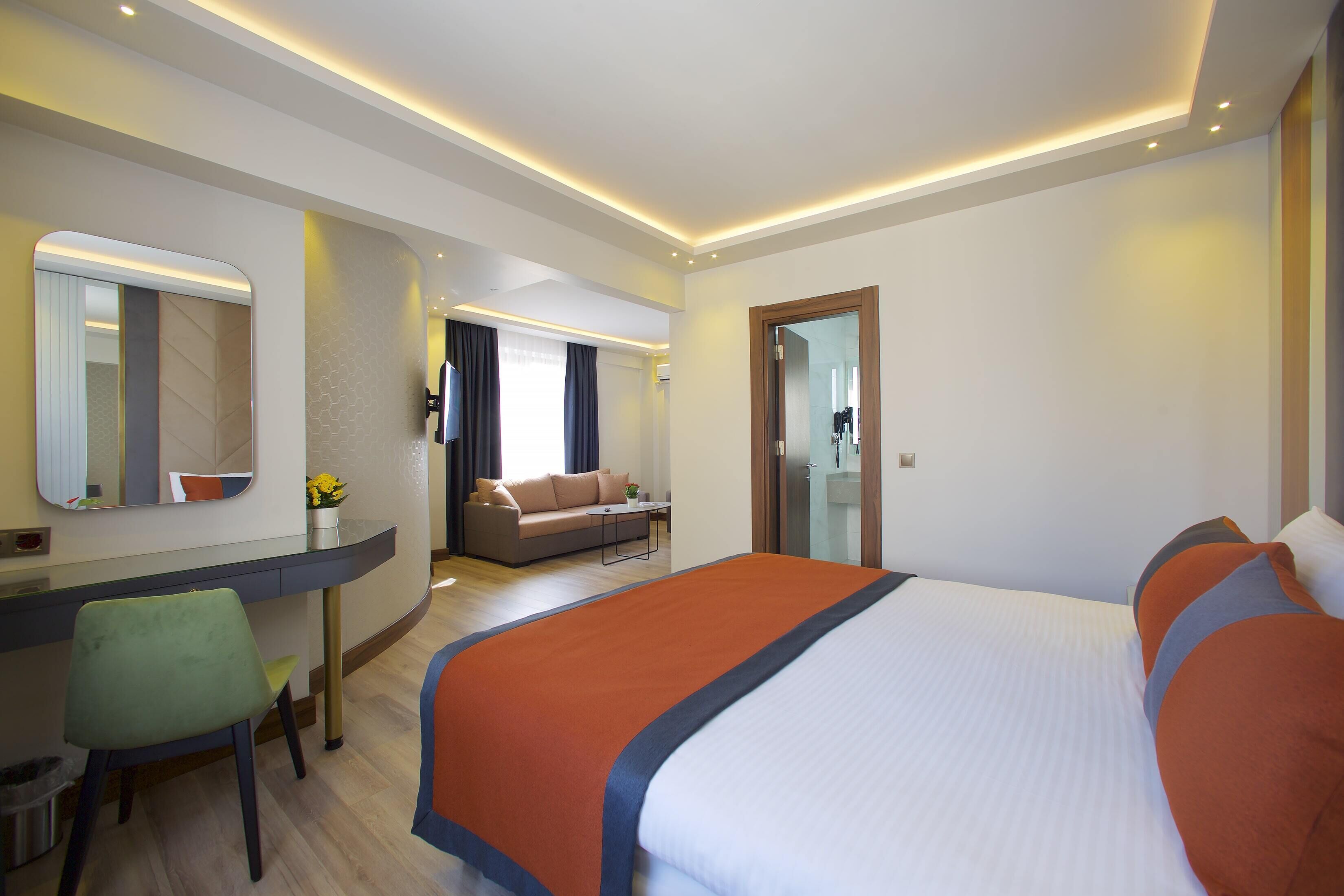 A hotel room with a large bed, a desk with a chair, a sofa, and a mirror.