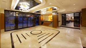 A modern lobby with a geometric floor design, glass doors leading to shops, and contemporary lighting fixtures. - Eyfel Hotel (Istanbul)