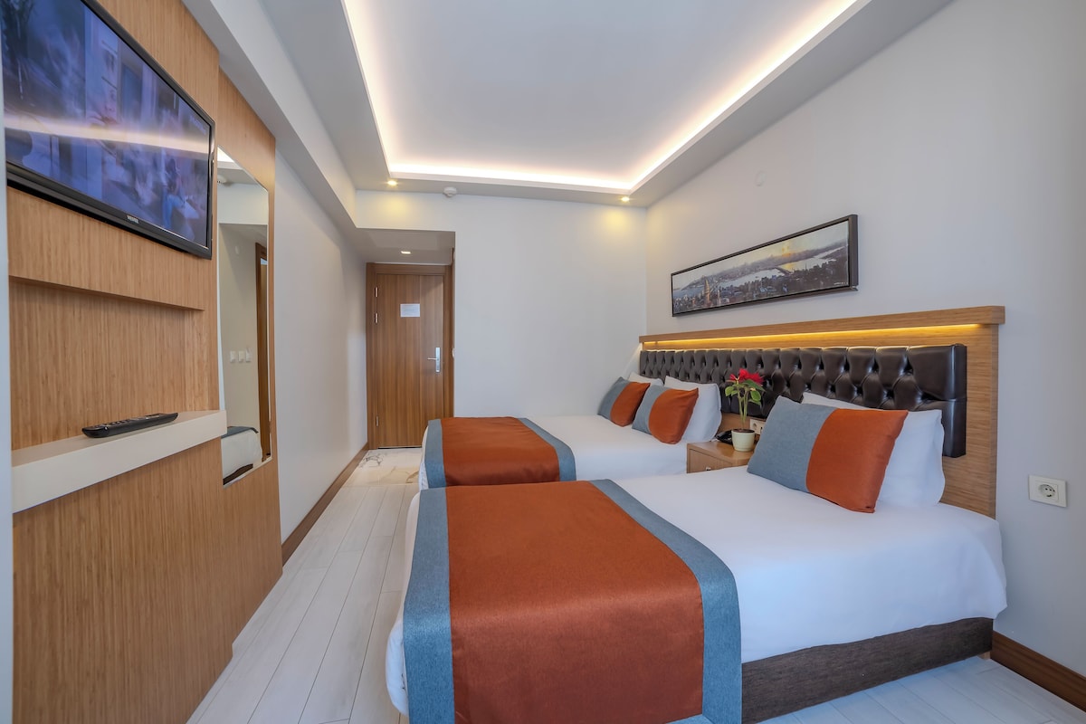 A hotel room with two beds, a TV, a wooden desk, and a framed picture on the wall.