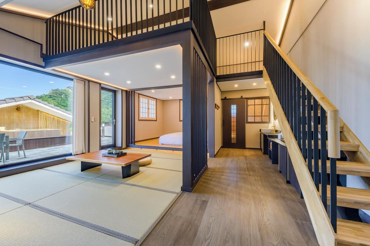 A modern interior with a wooden staircase, tatami flooring, and a view of a mountain.