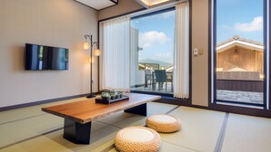 A modern interior with a wooden table, tatami mats, and a view of a building through large glass doors. - Hotel Harusida (Seogwipo)