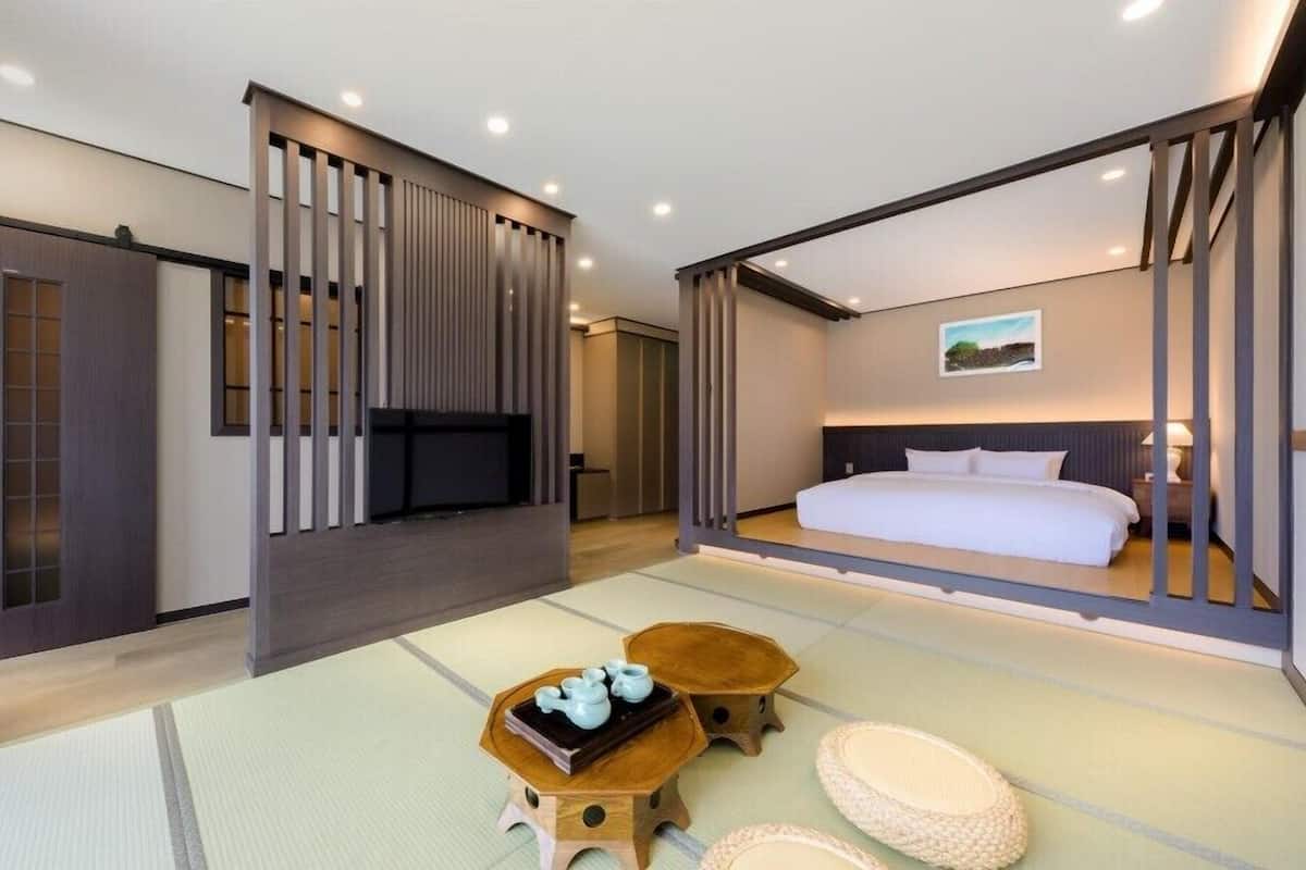 A modern hotel room with a bed, a television, a tatami mat floor, and traditional Japanese decor.