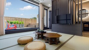 A modern living room with tatami mats, a low wooden table, and a TV. - Hotel Harusida (Seogwipo)