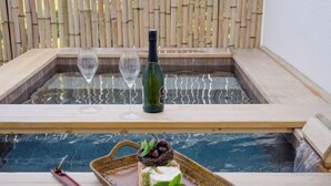 A hot tub with two glasses and a bottle, surrounded by a bamboo fence. - Hotel Harusida (Seogwipo)