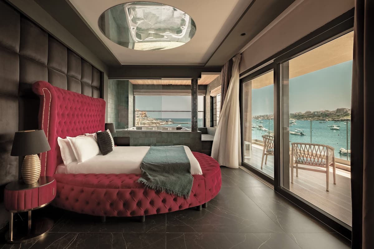 Quarto moderno com cama grande, vista para o mar e varanda com cadeiras de vime.