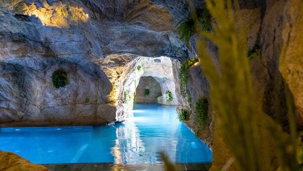A pool with a natural rock archway, surrounded by greenery. - Damare Resort & Spa (St. Paul's Bay)