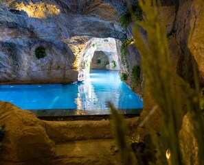 Une piscine agrémentée d’une arche naturelle en pierre, entourée de verdure.