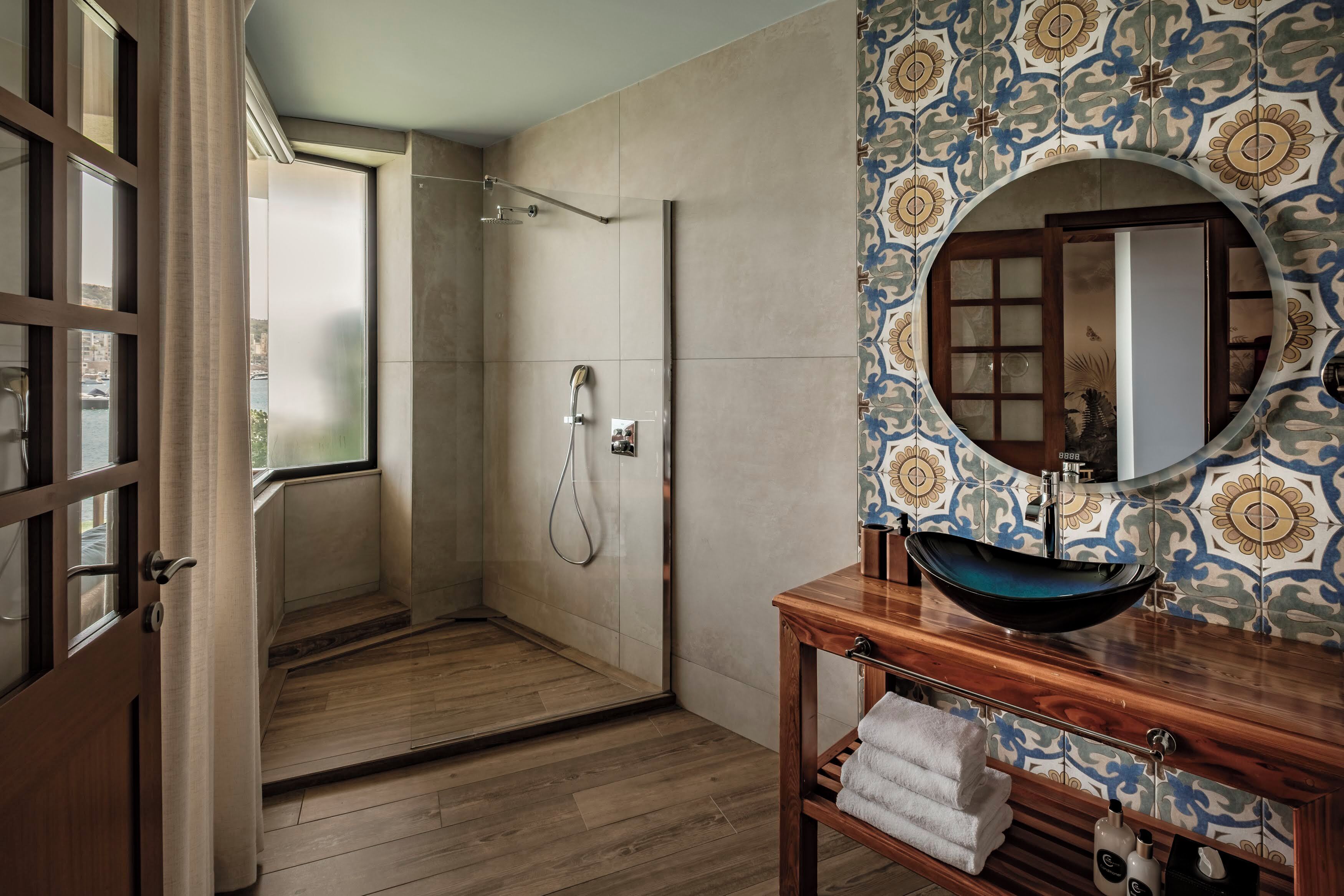 Ein modernes Badezimmer mit barrierefreier Dusche, einem Holzwaschtisch mit Aufsatzbecken und Wandfliesen mit Muster.