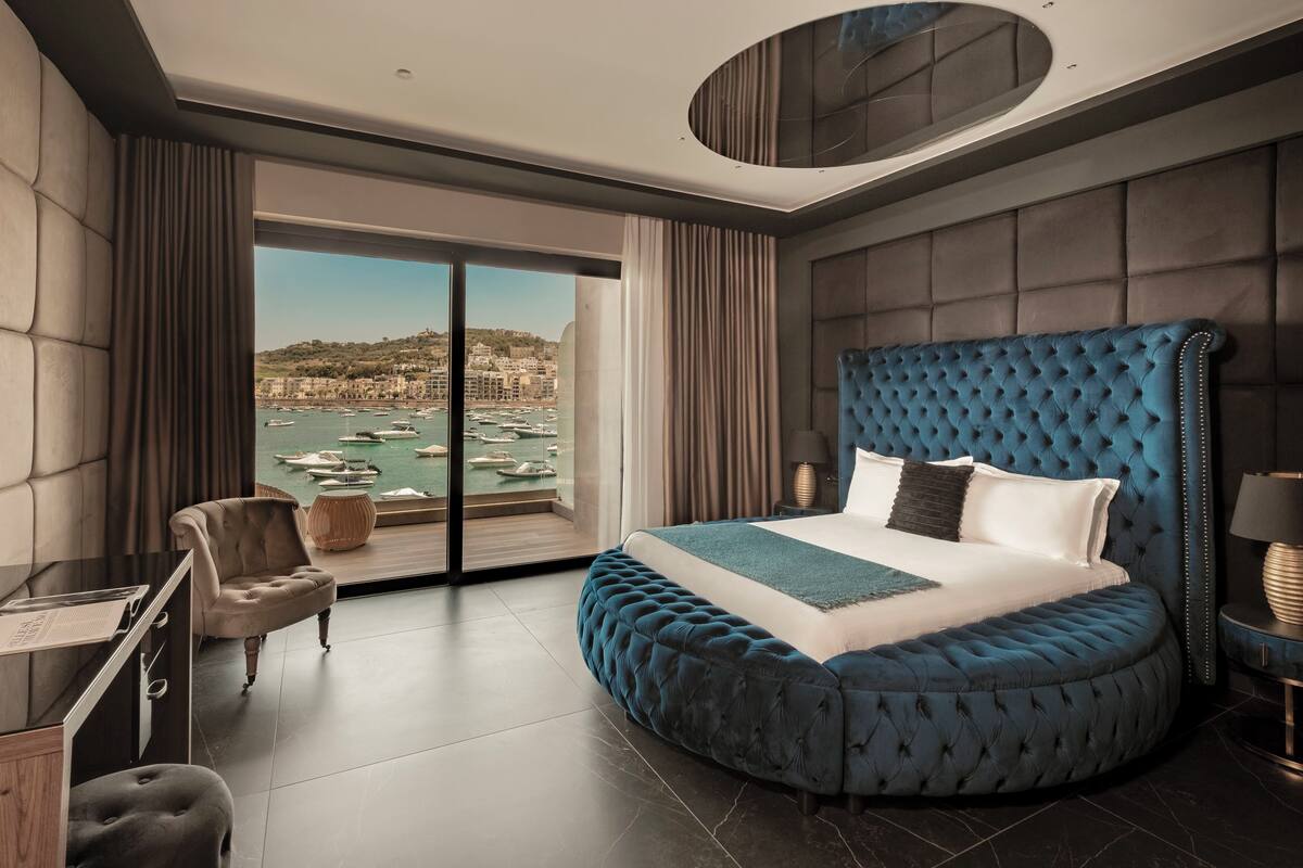 Quarto de hotel moderno com uma cama grande, uma escrivaninha e vista para um porto.