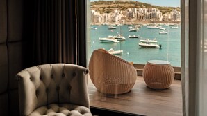 A room with a view of a marina, a tufted armchair, and two woven side tables. - Damare Resort & Spa (St. Paul's Bay)