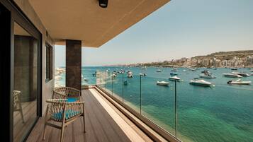 A balcony with a wicker chair, a view of a marina with boats, and a cityscape in the background.