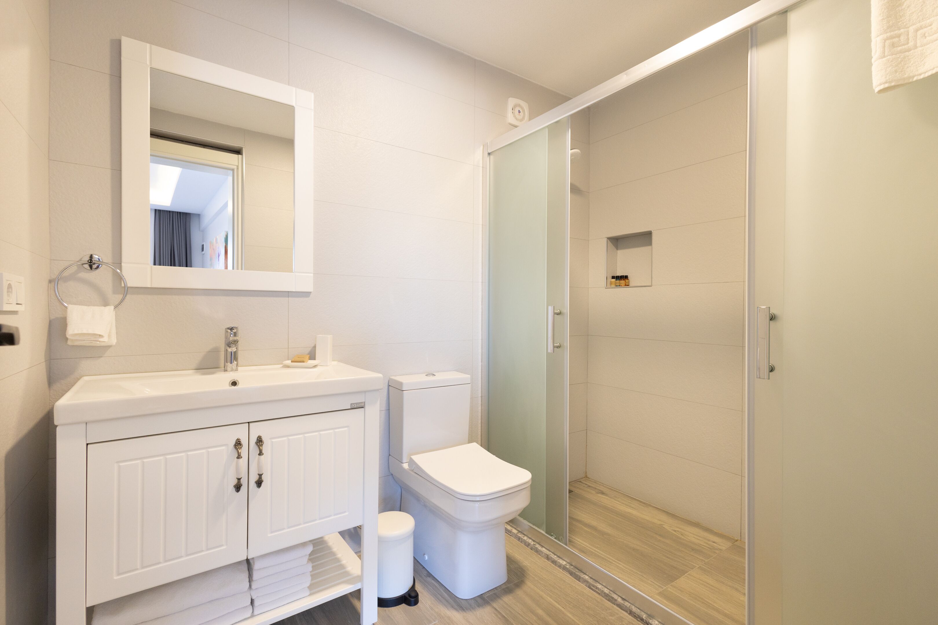 A modern bathroom with a white vanity, toilet, and glass shower enclosure.