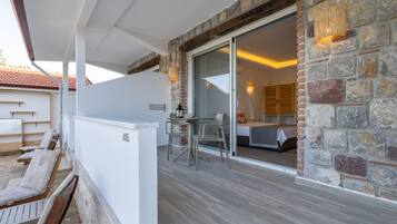 Un patio moderno al aire libre con un muro de piedra, un ventanal corredero que da a un dormitorio y una zona de estar con sillas y una mesa.