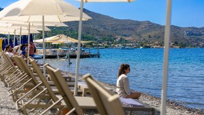 A beachside area with sun loungers and umbrellas, a dock, and boats in the background. - BASE Selimiye (Marmaris)