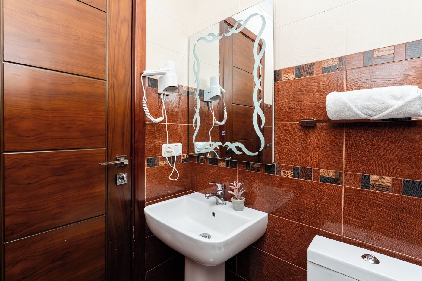 Een badkamer met een houten deur, een witte wastafel, een spiegel en een handdoekhouder.