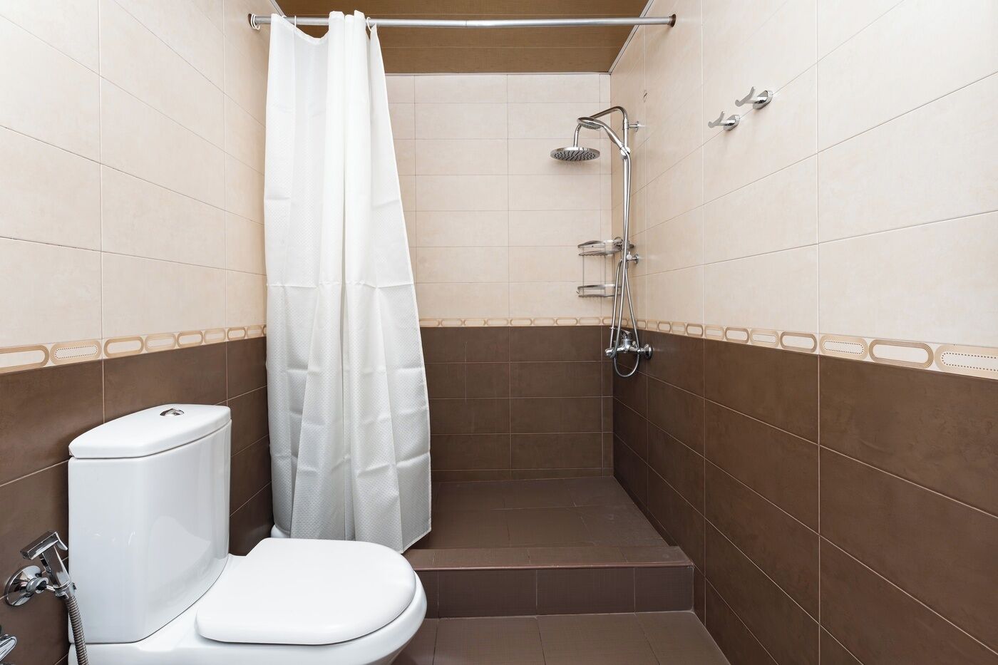 A small bathroom with a toilet, shower, and a white shower curtain.