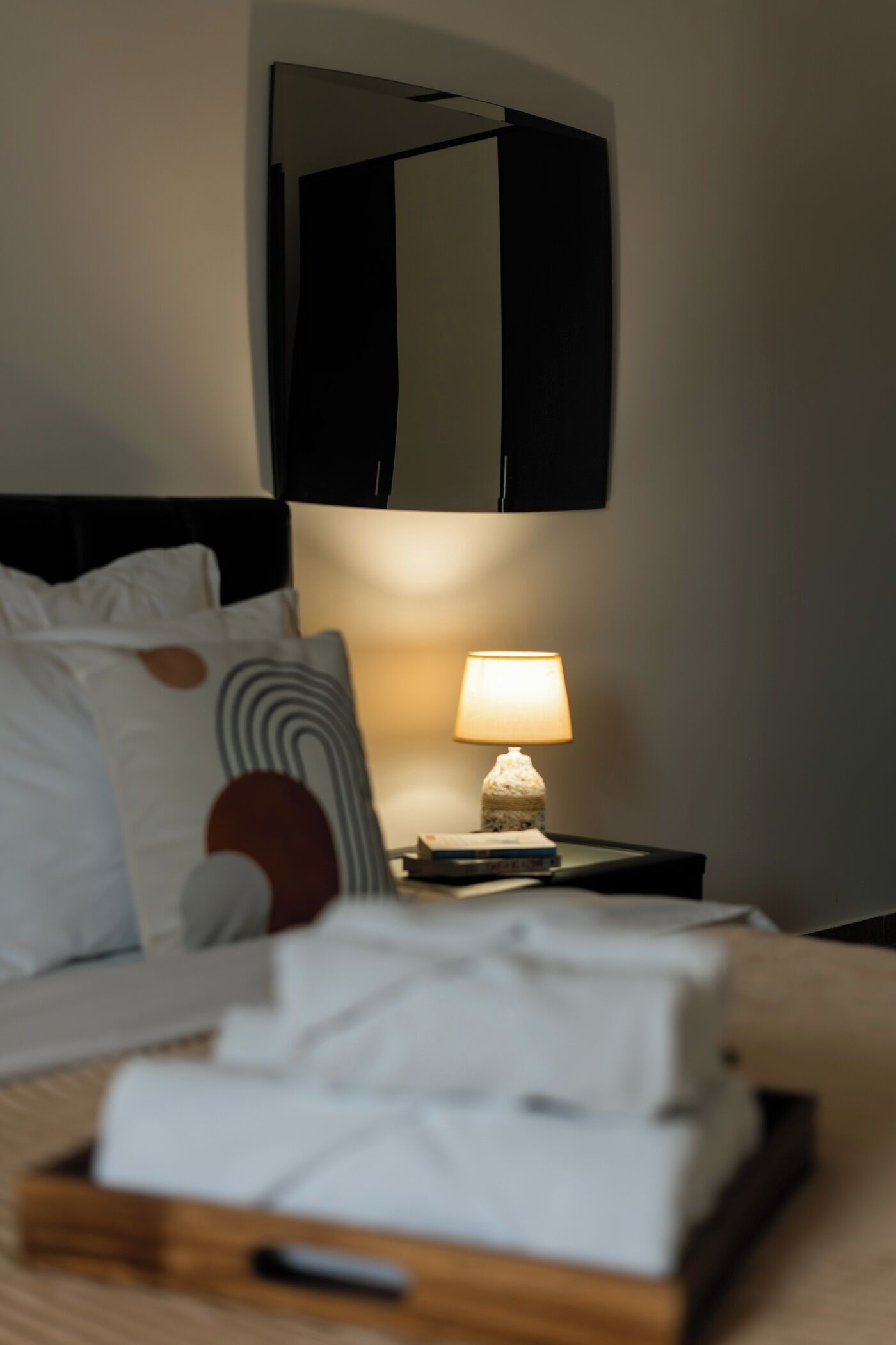 Cama bem arrumada com travesseiros, uma luminária de cabeceira e uma pequena caixa de madeira no criado-mudo.