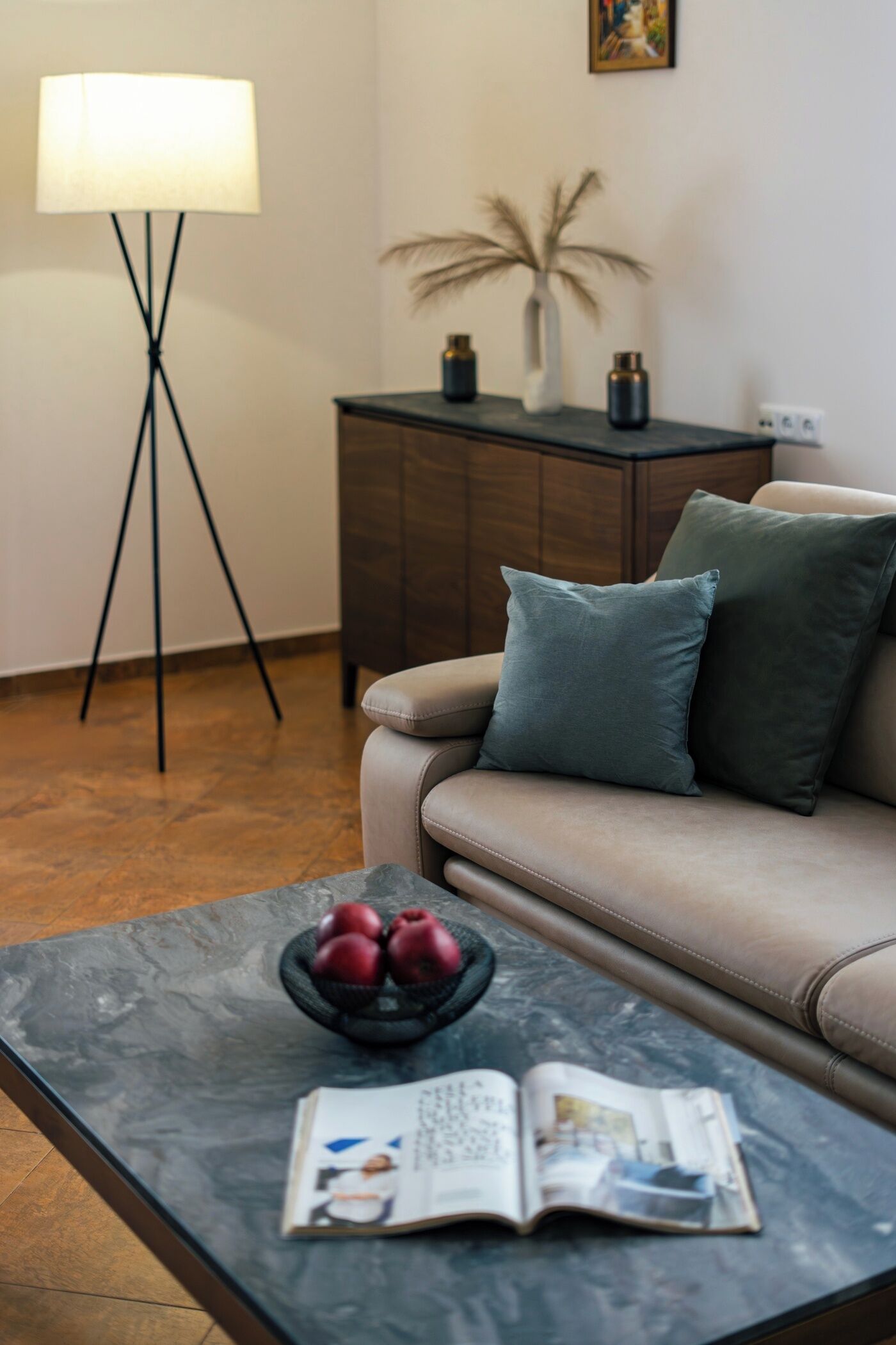 Un salon moderne comprenant un canapé, une table basse avec un saladier de pommes, une lampe et un petit meuble agrémenté d’objets décoratifs.