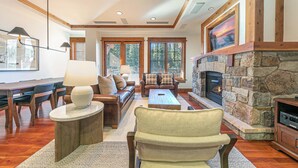 A spacious living room with a stone fireplace, wooden beams, and a large window.