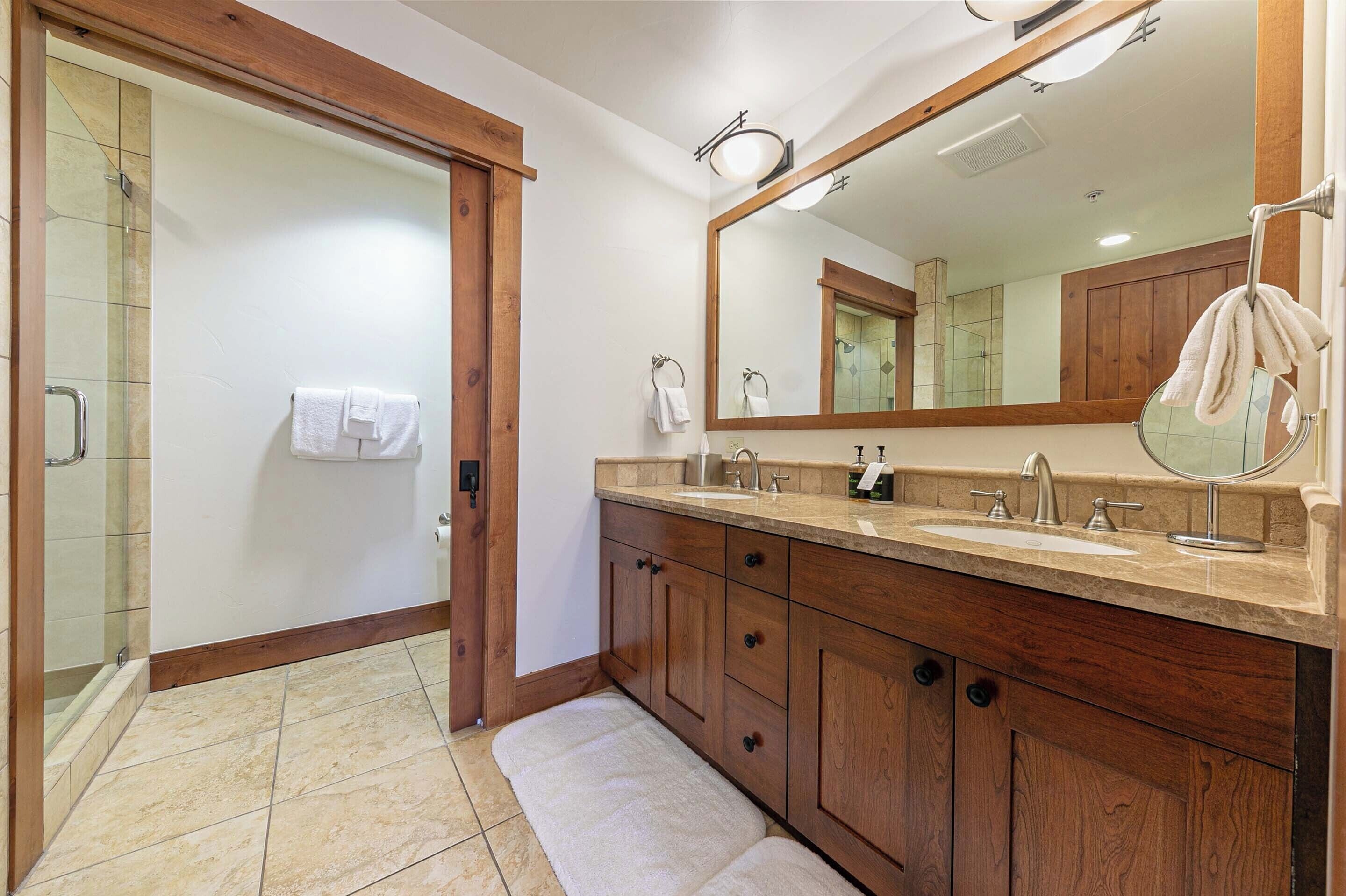 A bathroom with a wooden vanity, a large mirror, and a glass shower enclosure.