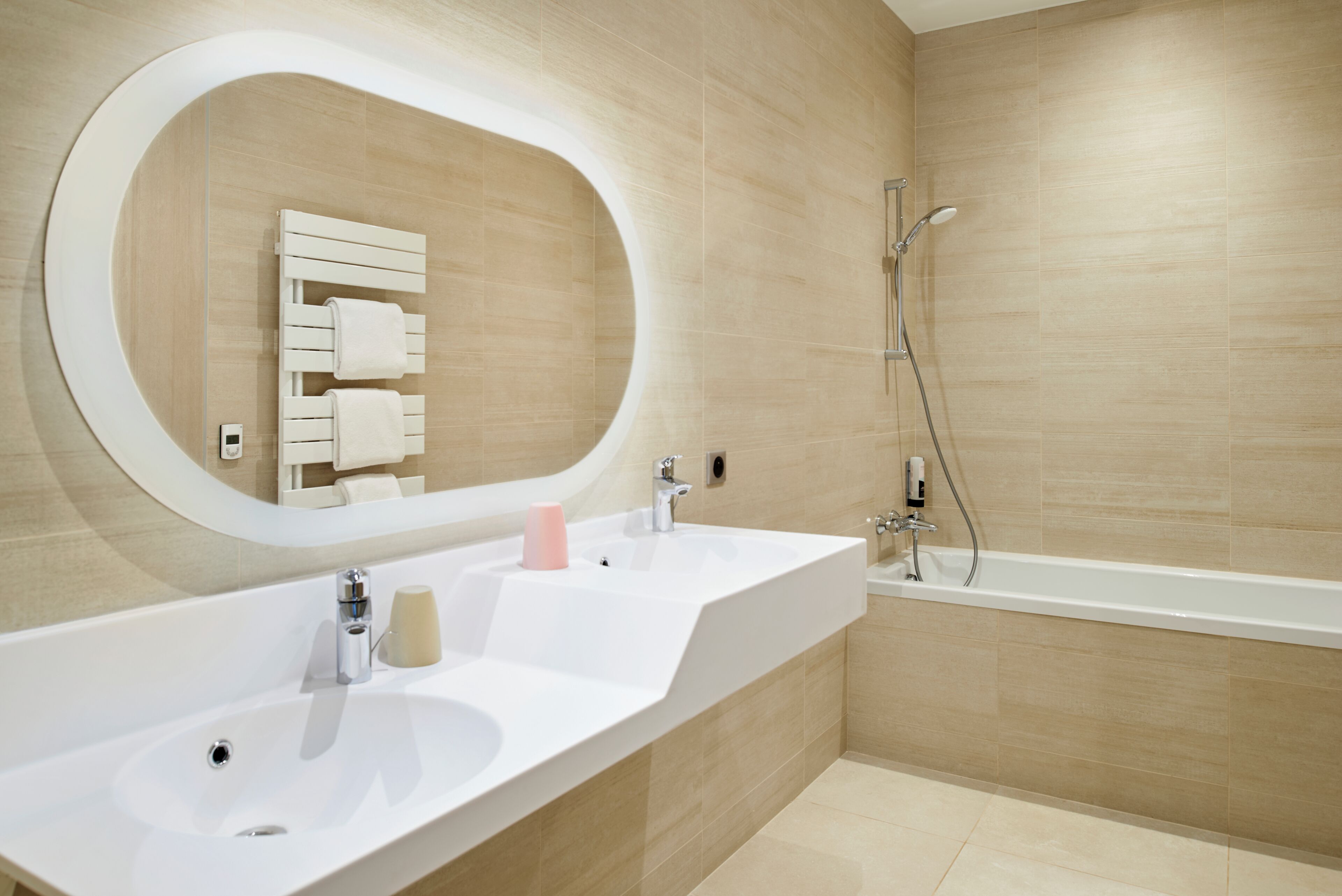 Un baño moderno con un espejo ovalado grande, dos lavamanos, una bañera y una ducha.