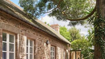 A stone building with a thatched roof, surrounded by lush greenery and trees.