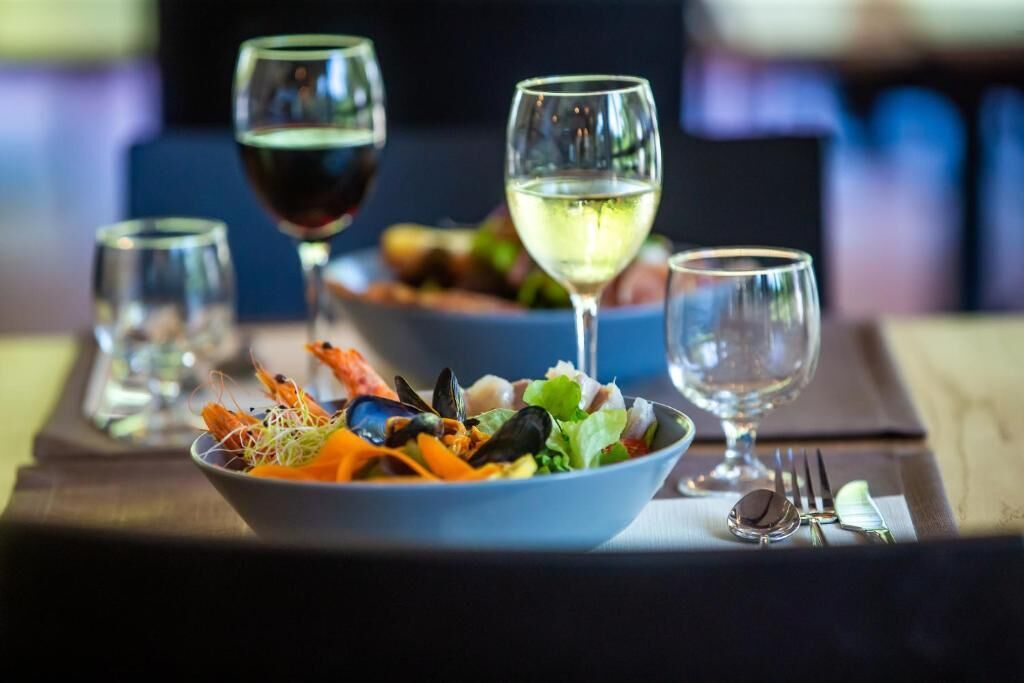 A dining table with a seafood salad bowl, two wine glasses, and cutlery.
