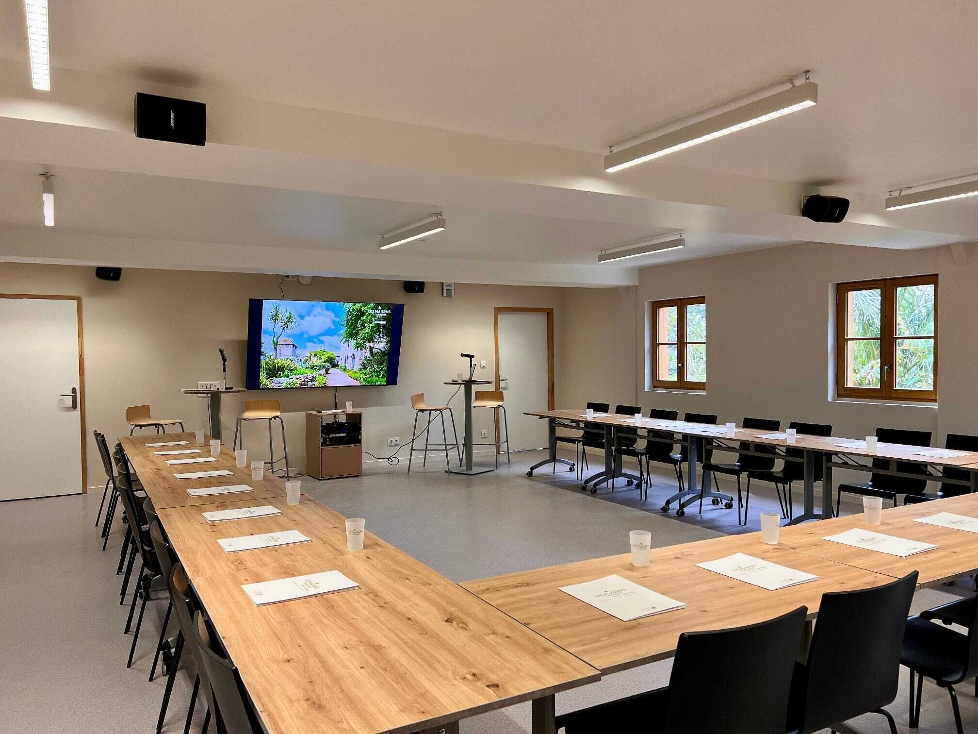 A conference room with long tables, chairs, a large screen, and a projector.