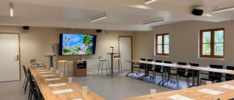 A conference room with long tables, chairs, a large screen, and a projector.