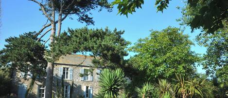 A stone building with a garden, surrounded by trees and plants.