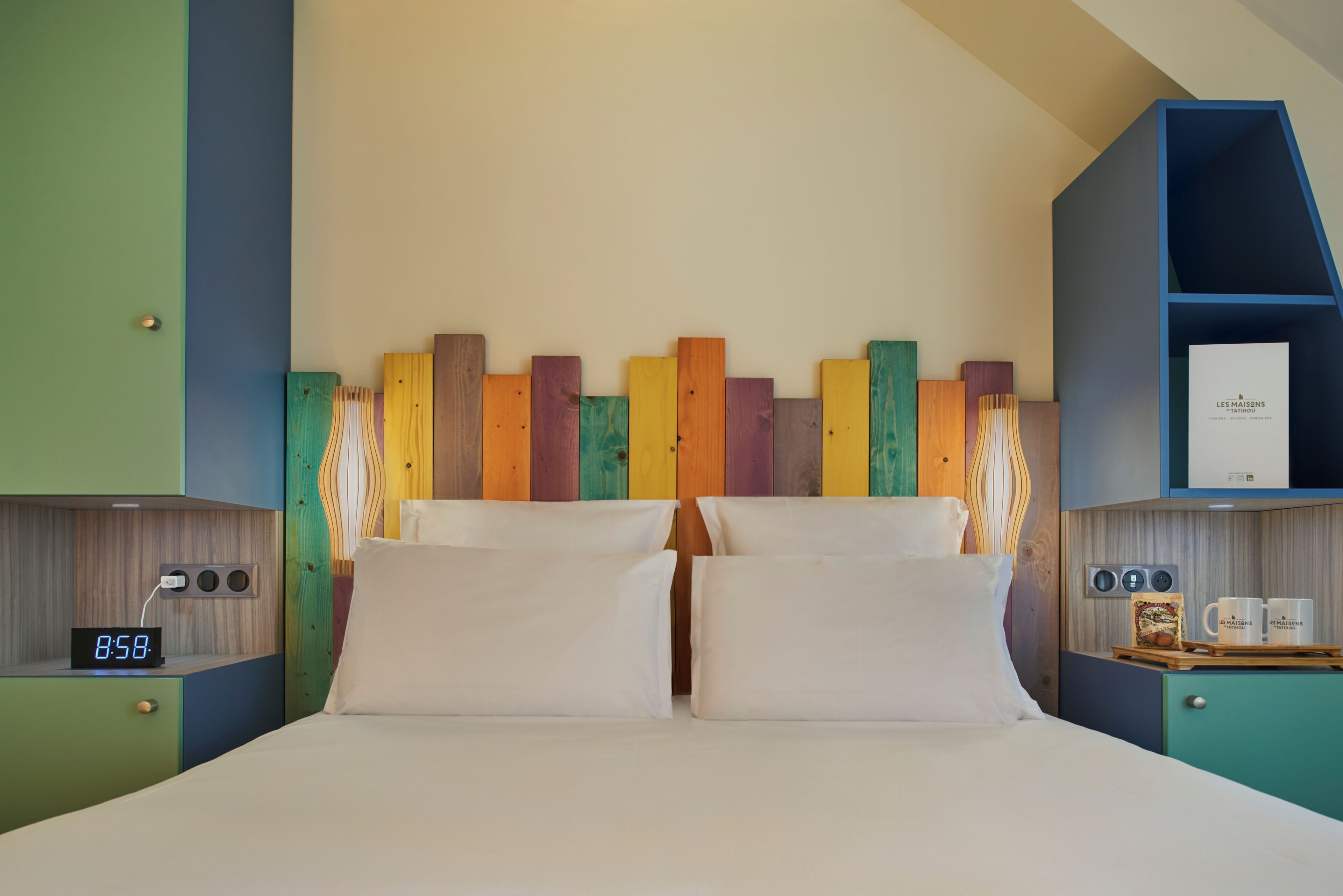 A bed with white bedding, a digital clock, and a colorful wooden headboard.