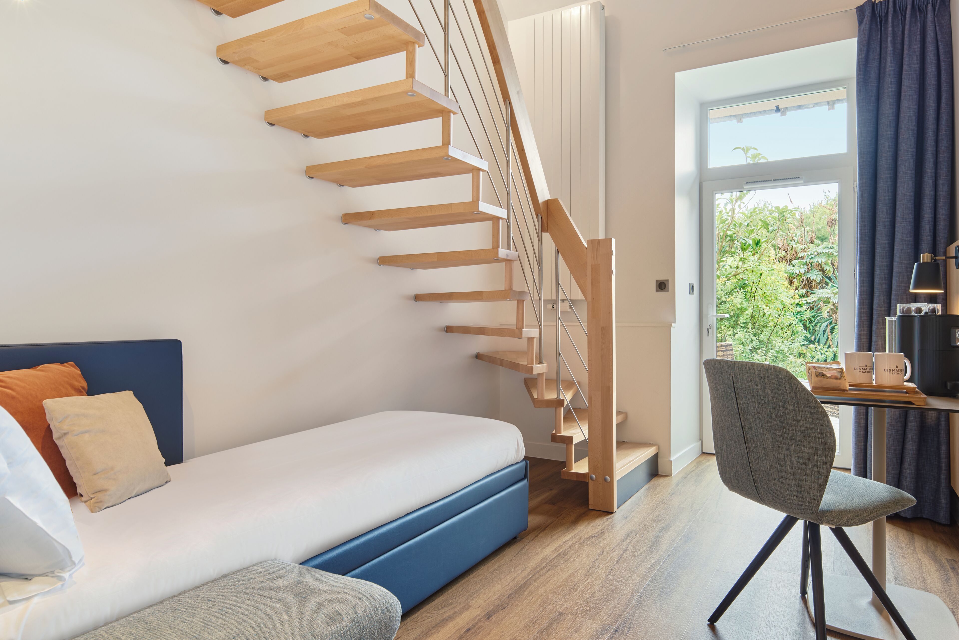 A modern room with a built-in bed, a wooden staircase, a desk with a chair, and a view through a large window.
