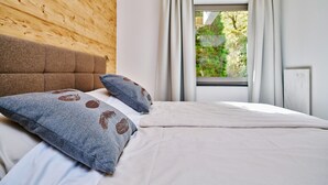 A bedroom with a wooden headboard, a large window with curtains, and a bed with a grey pillow. - Nice suite in Saalbach (Saalbach)