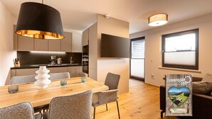 A modern kitchen with a wooden dining table, grey chairs, and a black pendant light.