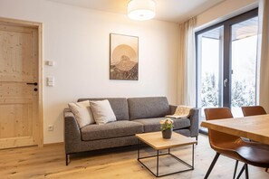 A modern living room with a grey sofa, a wooden coffee table, and a dining table with chairs. - Apartment with shared infinity pool (St. Martin am Tennengebirge)