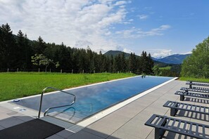 En udendørs swimmingpool med udsigt til bjerge og skov.