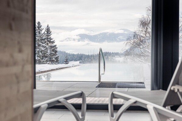 A view from a room with a glass door leading to a snowy outdoor area with a pool and mountains in the background.