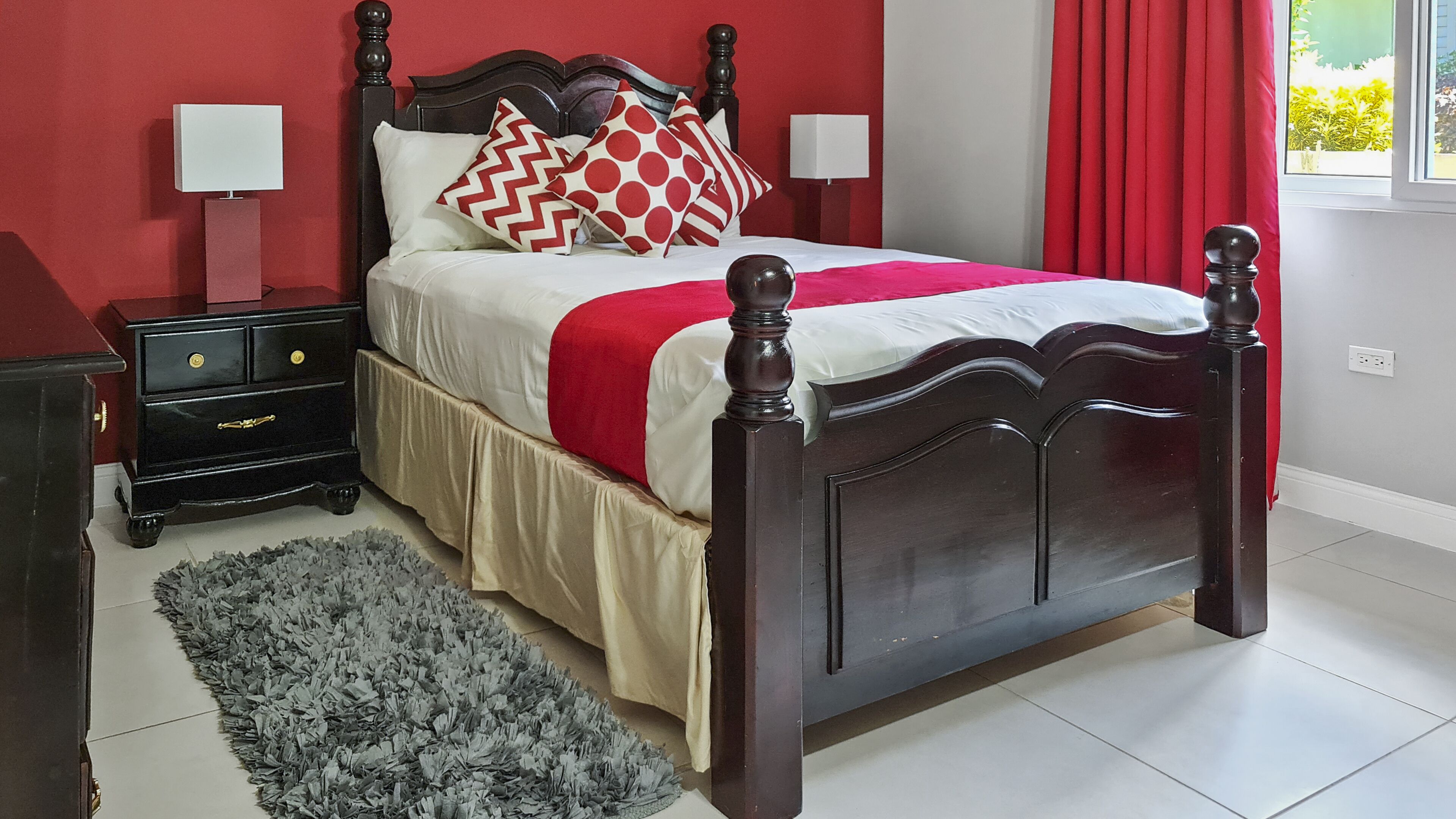 A neatly made bed with a red and white bedspread, a wooden headboard, and a bedside table with a lamp.