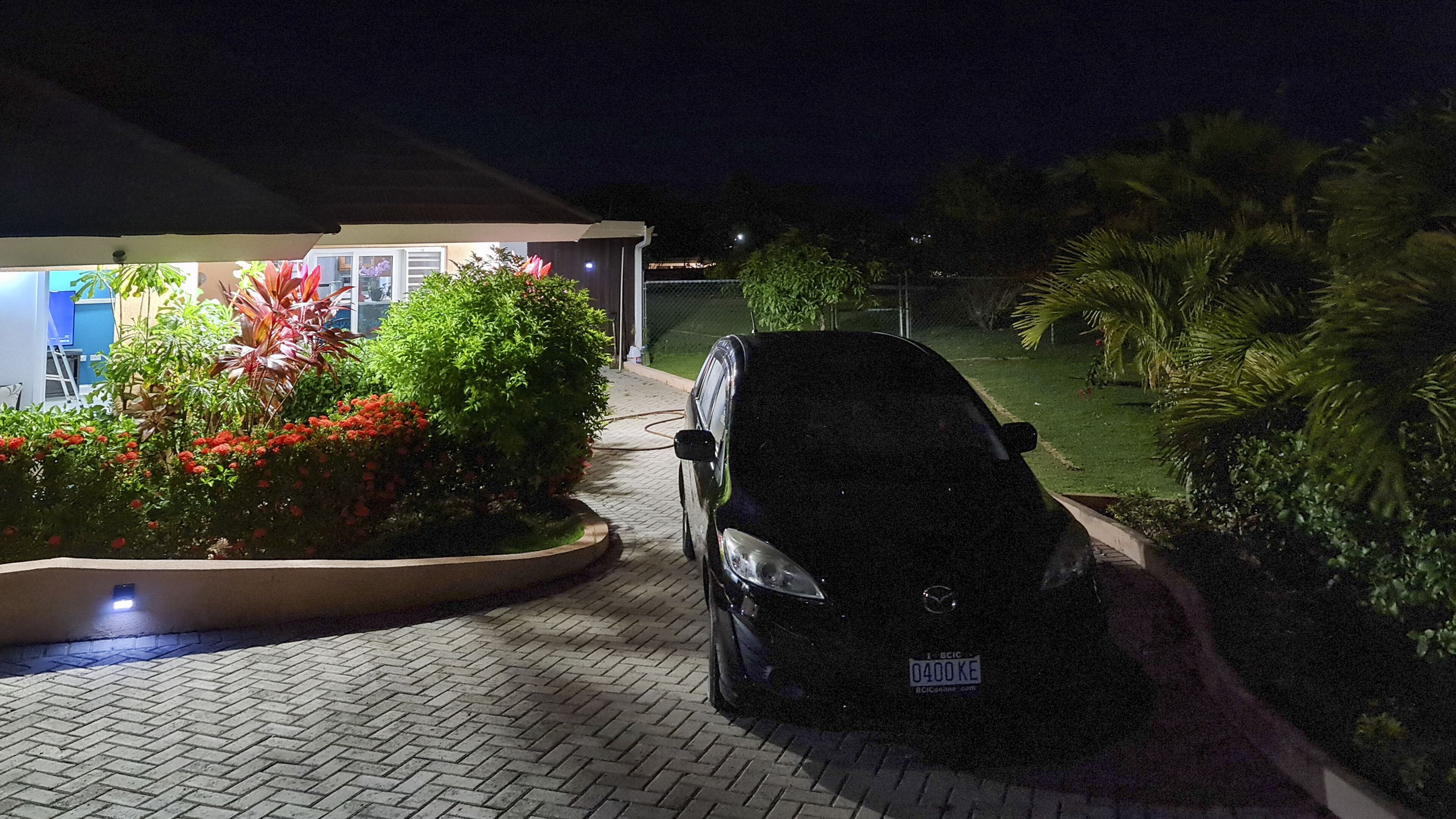 Une voiture garée dans une allée menant à une maison, la nuit, avec la maison en arrière-plan.
