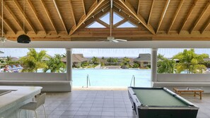 Un área de piscina cubierta con vistas a una piscina, sillas de descanso y una mesa de billar.