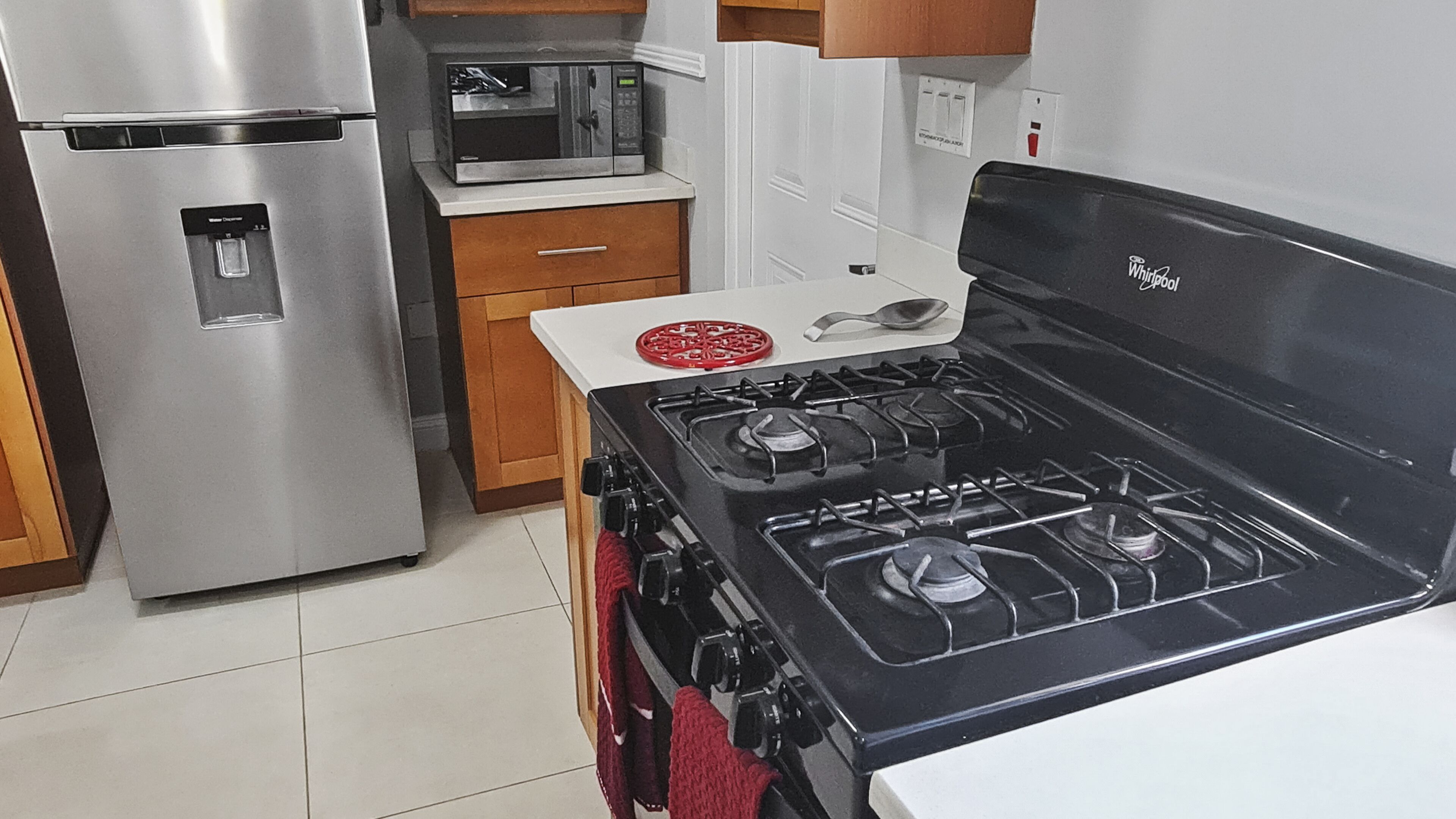 A kitchen with a stainless steel refrigerator, a microwave, a gas stove, and wooden cabinets.