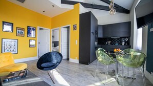 A modern living room with a yellow accent wall, a black chair, and a glass dining table with chairs. - Le Loft de St Jean - 2 bed and 2 bath (Cannes)