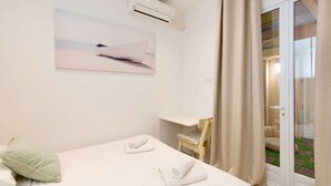 A hotel room with a bed, a desk, a chair, an air conditioning unit, and a sliding glass door leading to an outdoor area. - St Nicolas - Cosy "Cabane de plage" avec A/C & Patio à 10 min to Palais  (Cannes)