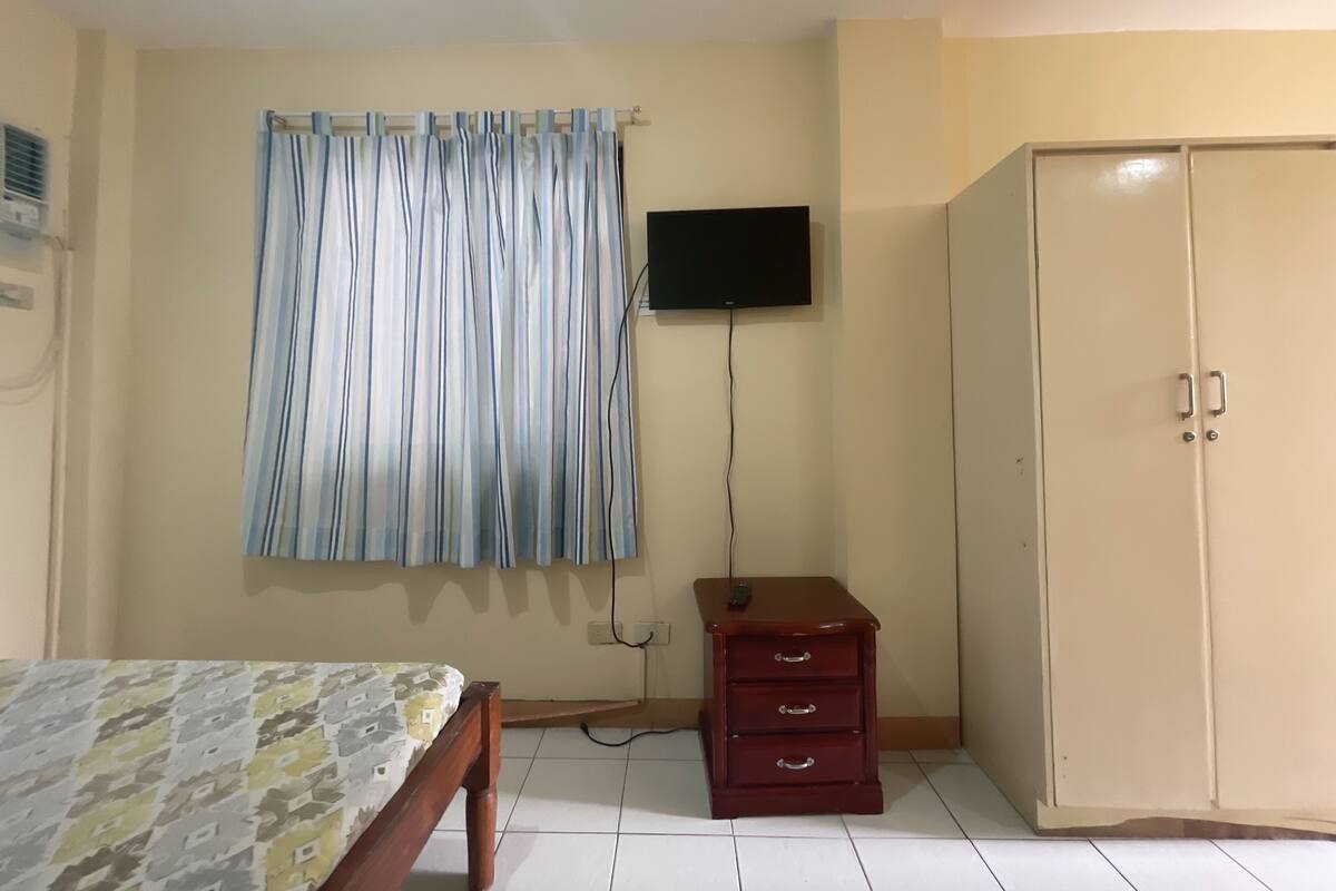 A room with a bed, a wardrobe, a TV mounted on the wall, and a curtain.