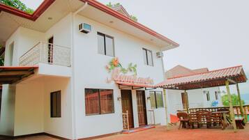 A two-story building with a balcony, a covered patio with furniture, and a sign that reads "Kumamela".