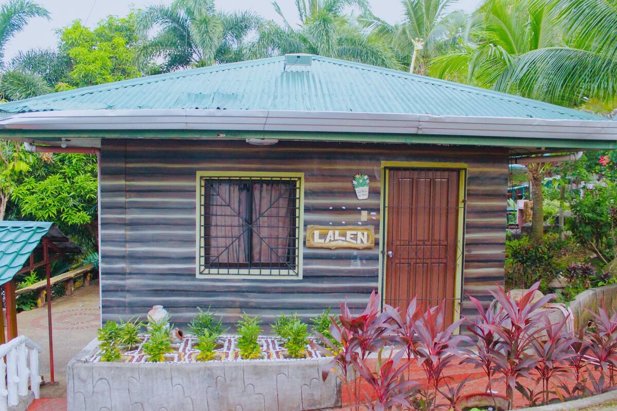 A small wooden building with a corrugated metal roof, a window with a metal grid, and a door. There is a sign above the door that reads "Lalen".